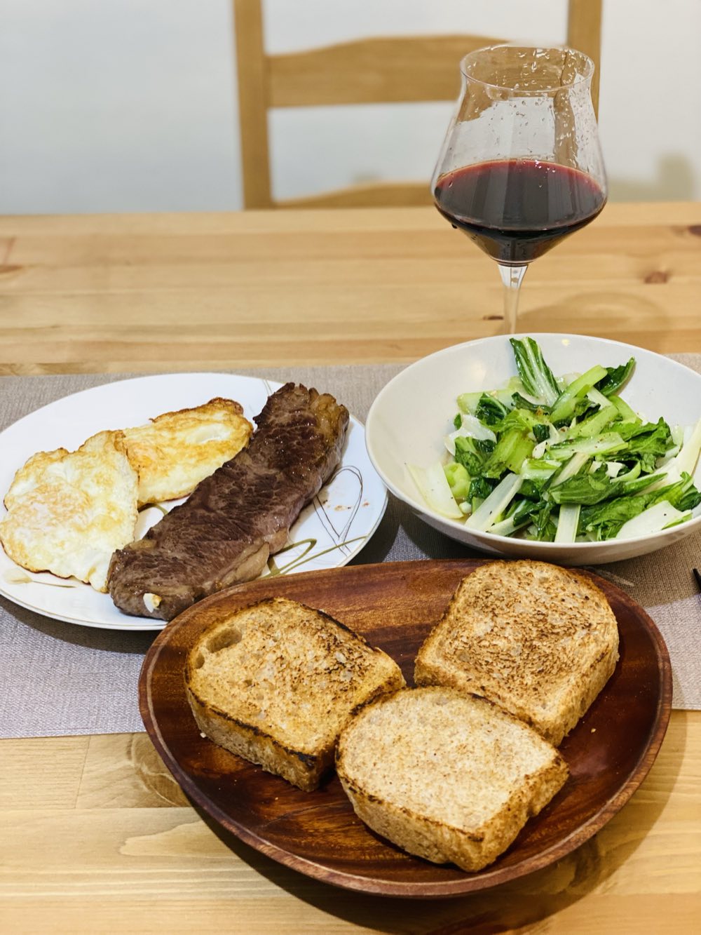 餐桌上的一頓飯：木盤裡的全麥吐司、煎蛋牛排、青菜與一杯紅酒