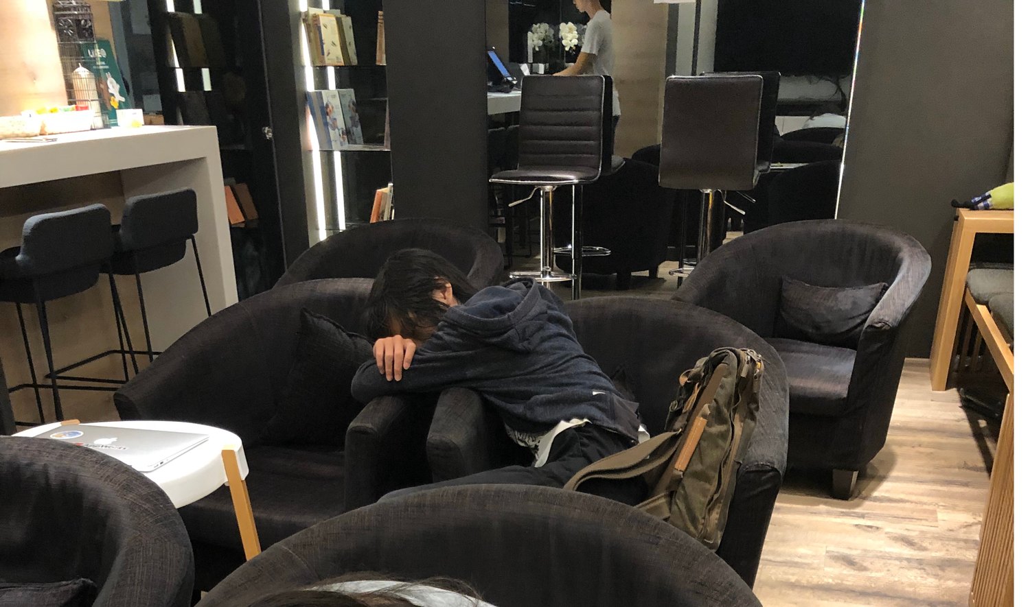 一個孩子累到趴在青旅的扶手椅上睡著，旁邊放著背包，不遠處的桌上還開著筆電。