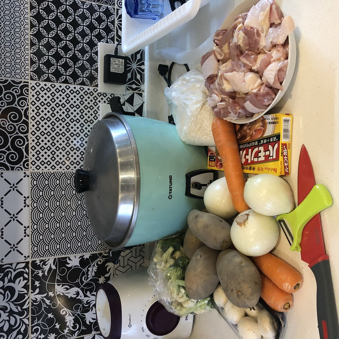 四個孩子在青旅裡一起準備食材煮咖哩，桌上有電鍋、蔬菜、雞肉與咖哩塊。