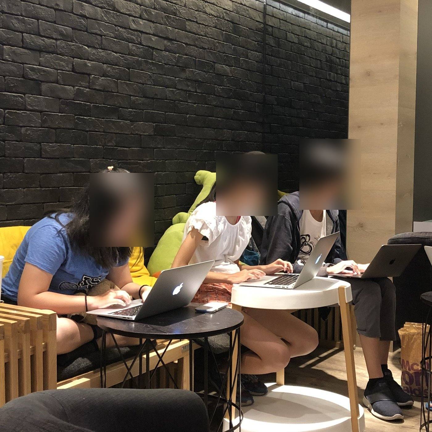 三個孩子在青旅並排坐著，各自對著筆電工作，臉部已模糊處理。