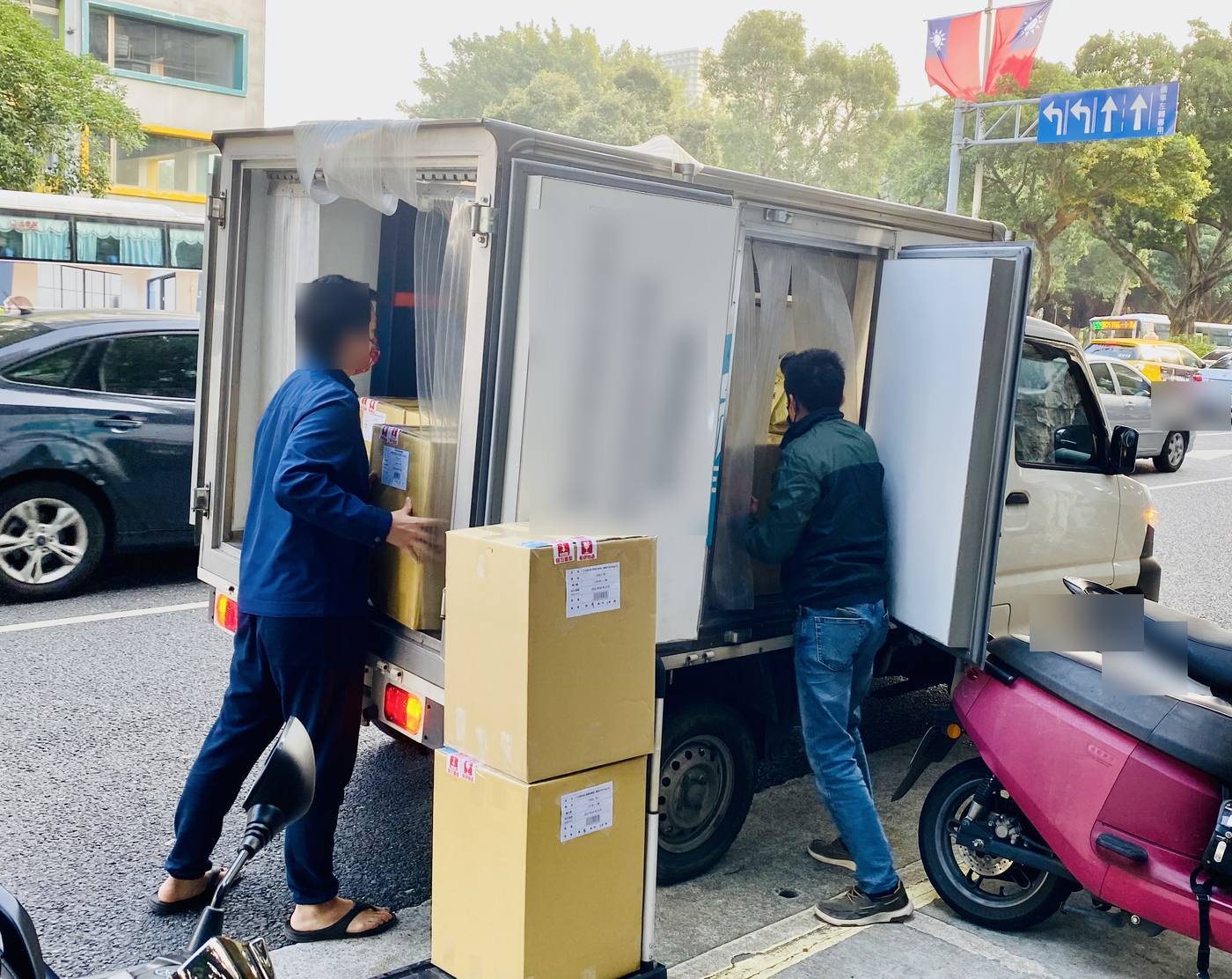 清晨的接貨現場：冷藏車開著門，紙箱堆在人行道上，兩個人正在搬貨。