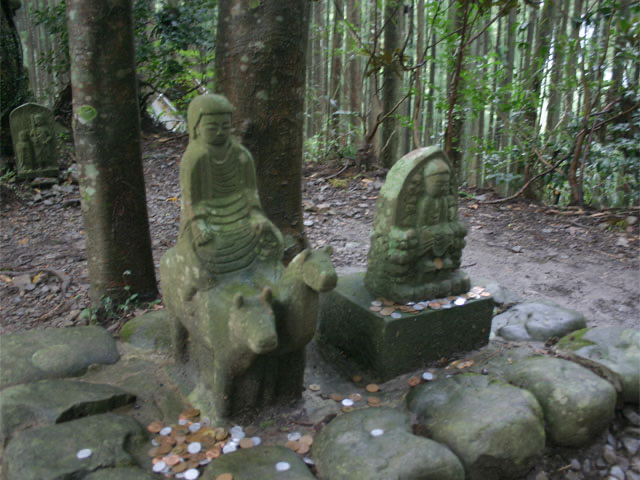 熊野古道沿途的牛馬童子石像，苔痕斑斑，周圍散落著參拜者留下的硬幣。
